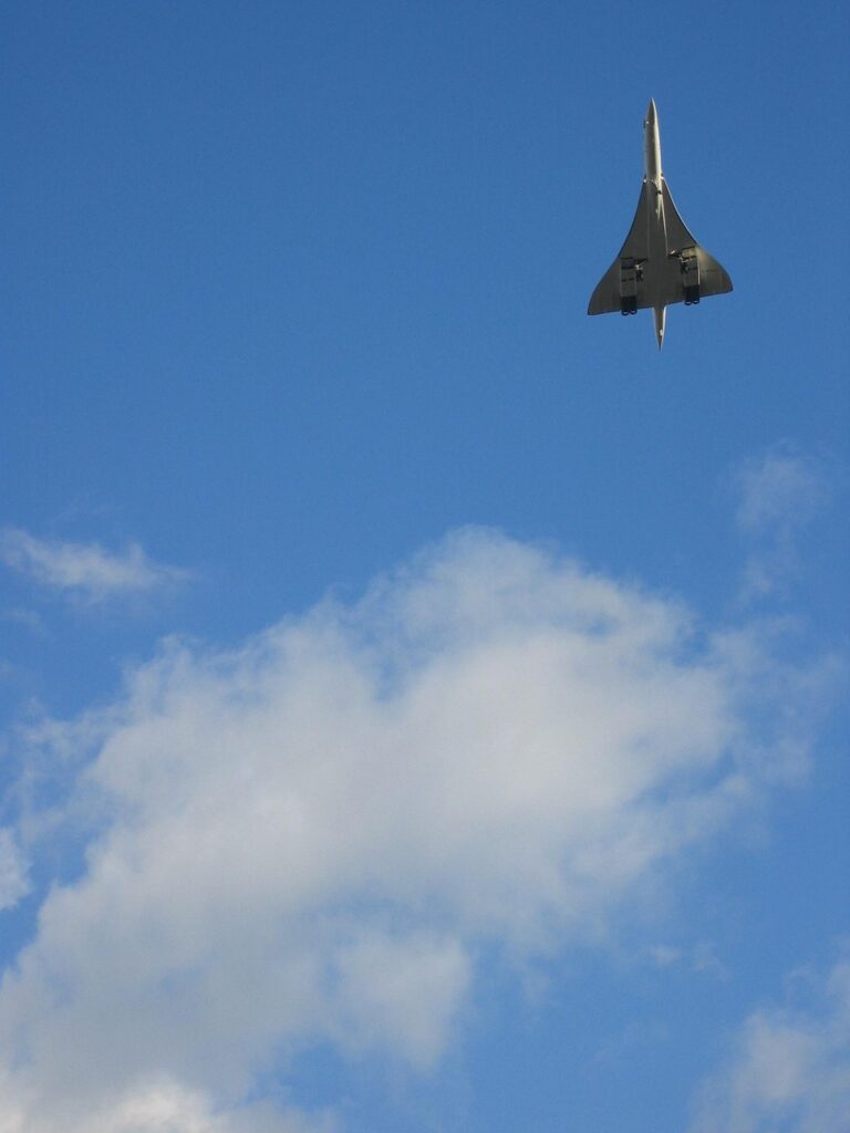 Concorde flying vertically against a clear blue sky with landing gear extended.